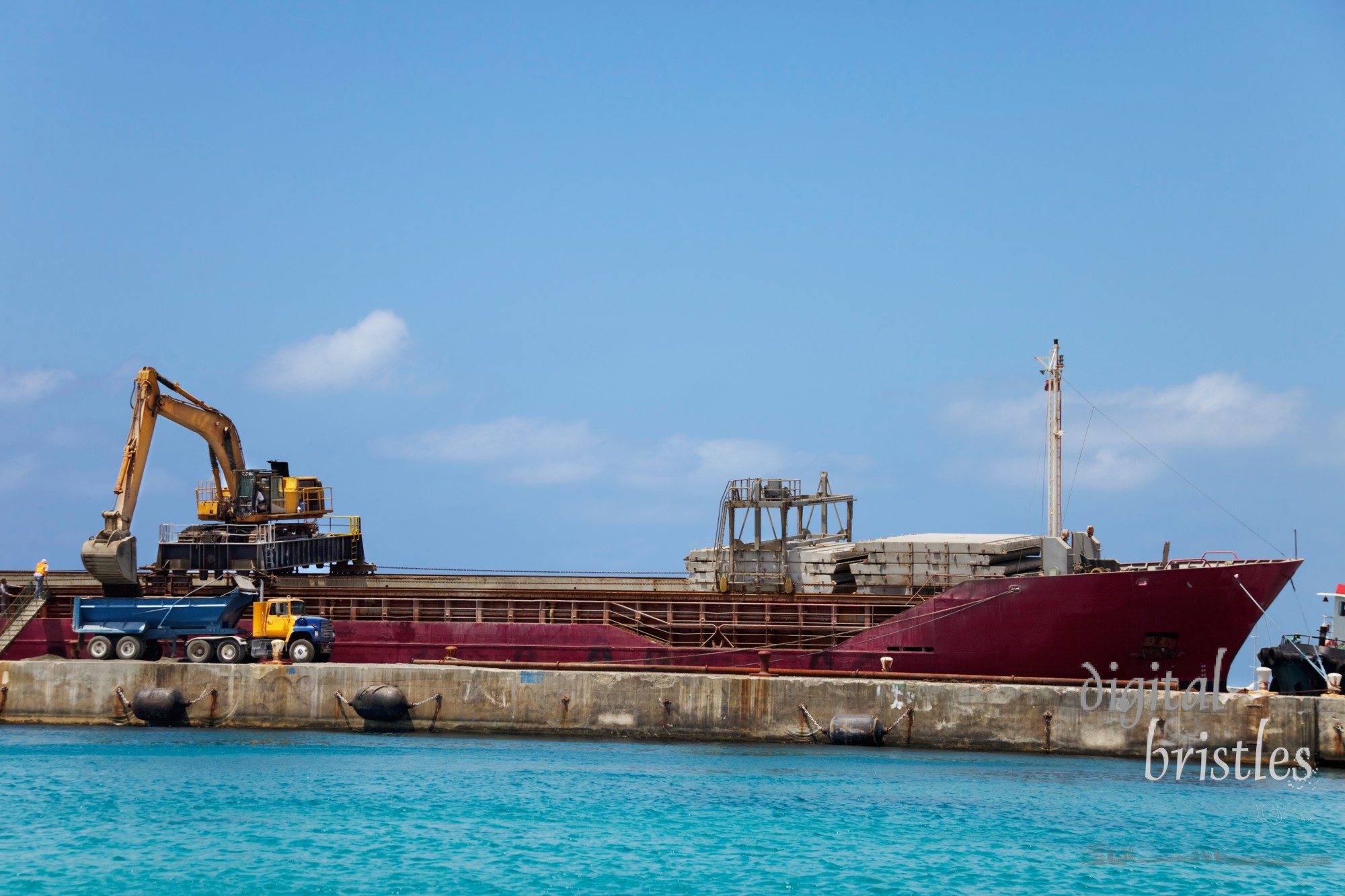 Excavator on top of a docked ship offloads dirt into a dump truck