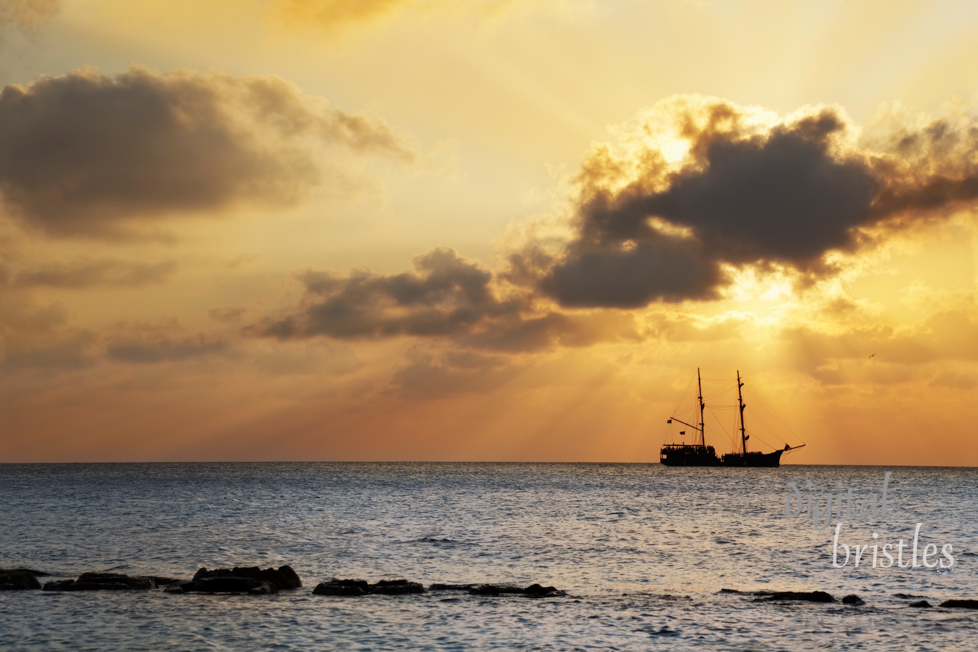 Old-fashioned boat passing by the setting sun off Seven Mile Beach, Grand Cayman