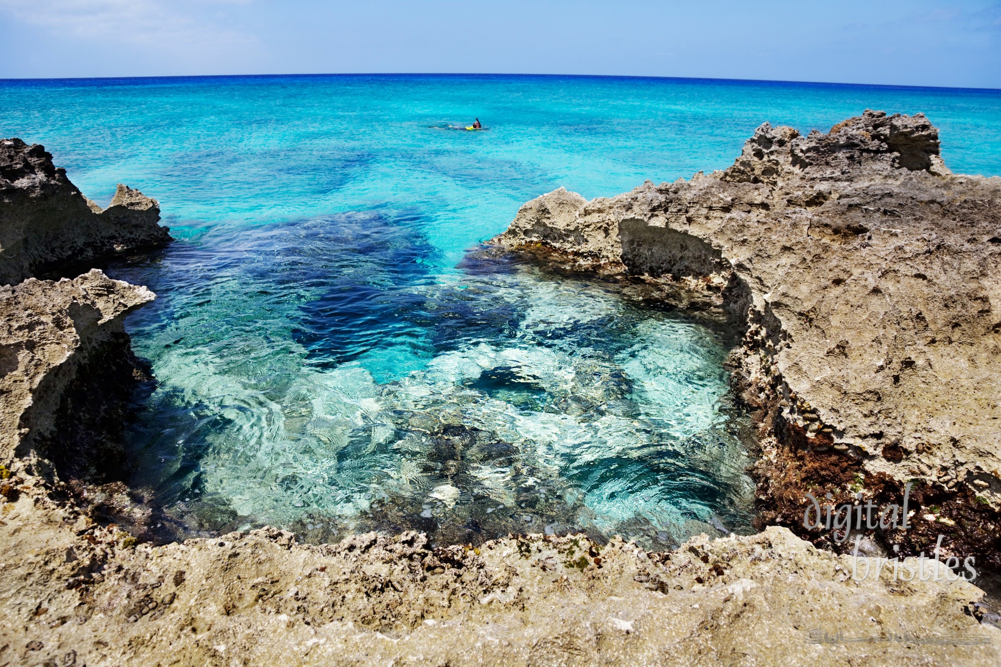 Man explores the reef off the rocky (Ironshore formation) areas of Smith Cove, Grand Cayman. Slight curve to the horizon