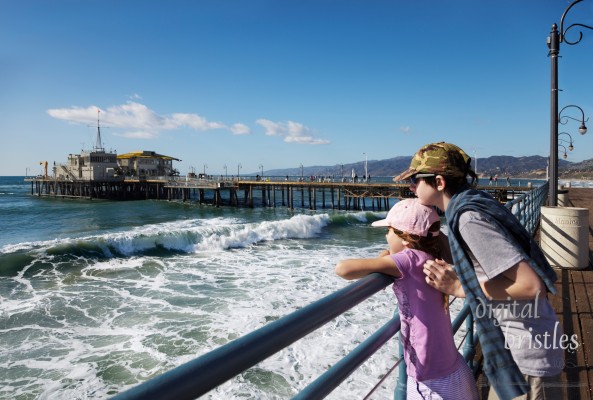 Brother holds his sister as they watch the waves from the end of the pier