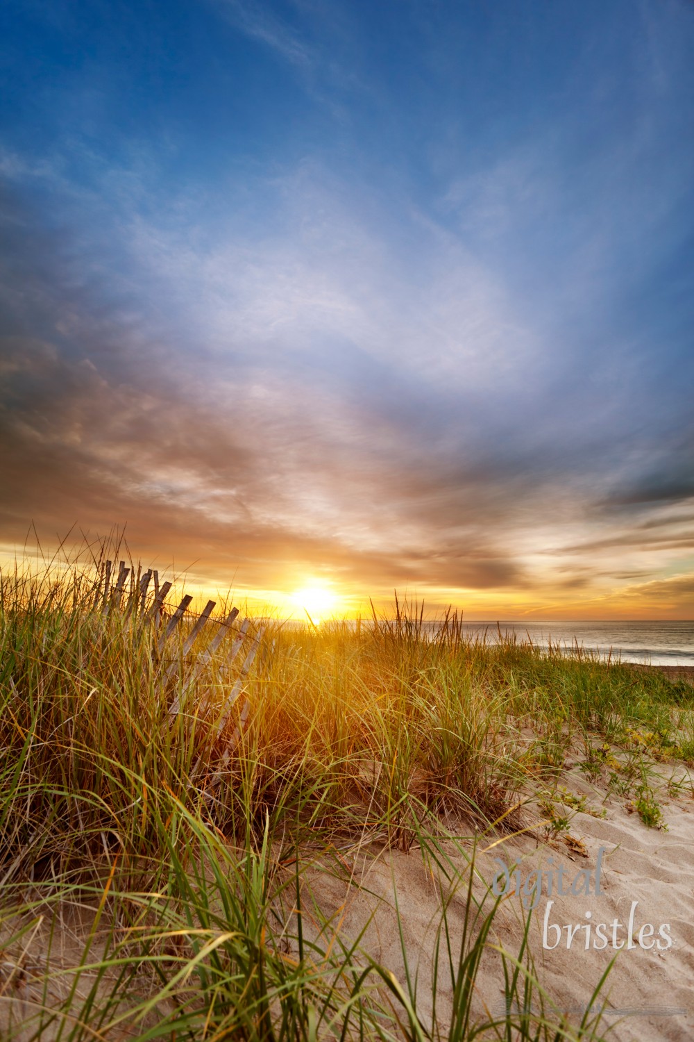 Sun rises over the dunes and a collapsing wooden fence on a Maine beach